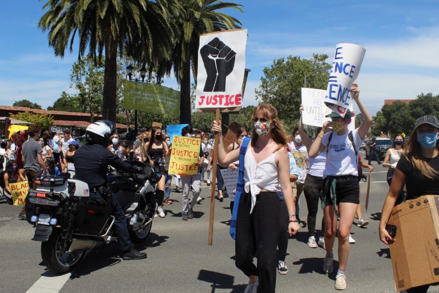 JUSTICE.+A+large+group+of+protesters+pass+by+a+police+officer+during+a+Black+Lives+Matter+March+near+Town+and+Country+Village+in+Summer+2020.+Photo+by+Corie+Jiang.