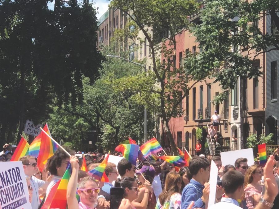 2019 New York Pride parade attendees walk down the street waving rainbow flags. Photo by Ash Mehta