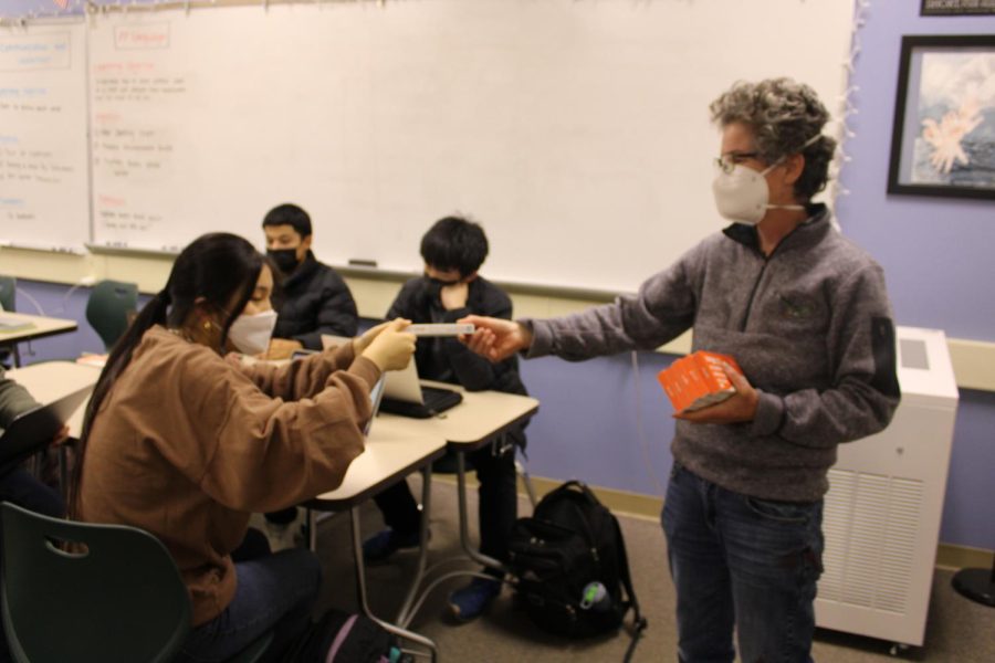 A substitute teacher distributes at-home COVID-19 test kits to students on Wednesday in an AP English Language and Composition class. Rising case numbers and the recent Omicron variant are causing safety concerns among some students and staff members. Junior Anjali Akkaraju said she believes a transition to online learning, though undesirable, is necessary. “I don’t want school to be back online, but I’m just confused why we’re not,” Akkaraju said. “They gave us two rapid tests, which is good because they’re sold out everywhere.”  Photo: Lauren Wong
