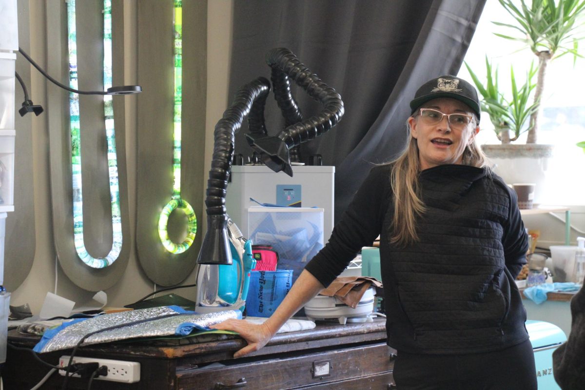 De La Garza in her studio at Cubberley standing on front of old light tubes that are covered with trash wrappers that all match a specific color scheme.